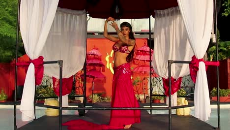 elegant, young and sexy belly dancer in red dress, performing under an arabian gazebo at the resort