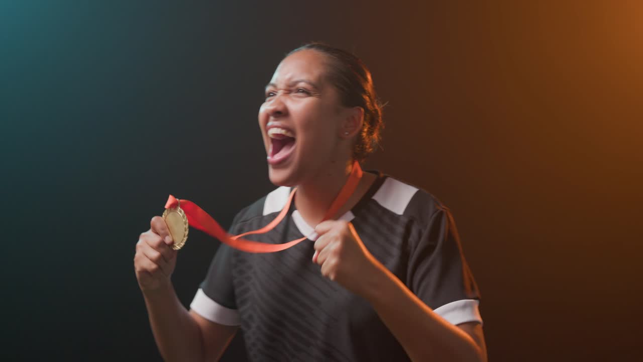 Donna afroamericana che ride e festeggia la vittoria in studio, con una medaglia d'oro e una maglia sportiva.