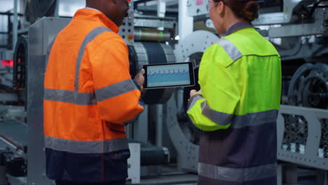 focused partners discussing charts on modern tablet computer at huge factory.