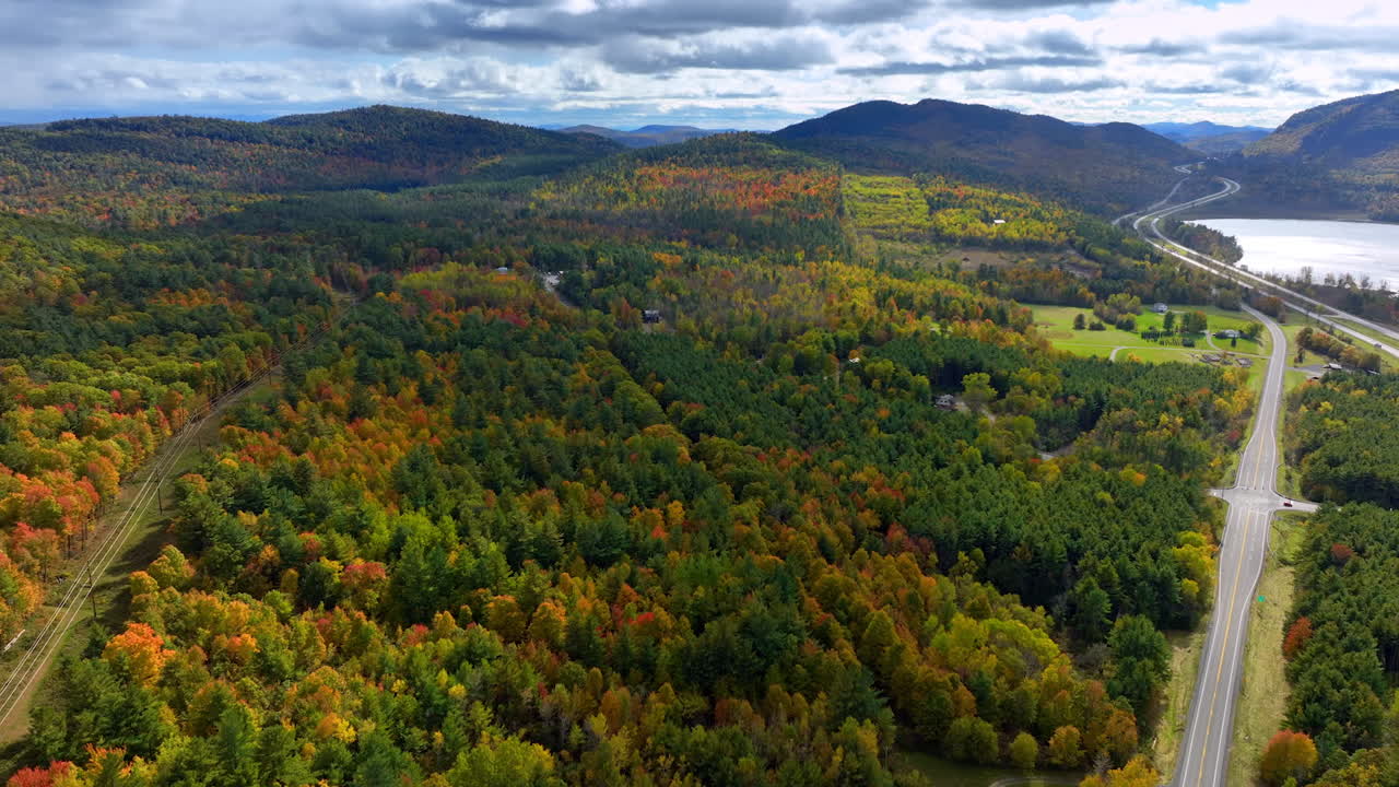 Rising over the lush woodlands in the north of New York state. Highway crosses the landscape leading to the lake. Autumn season in USA.