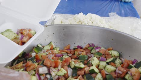 scooping fresh vegetable salad into a takeout container