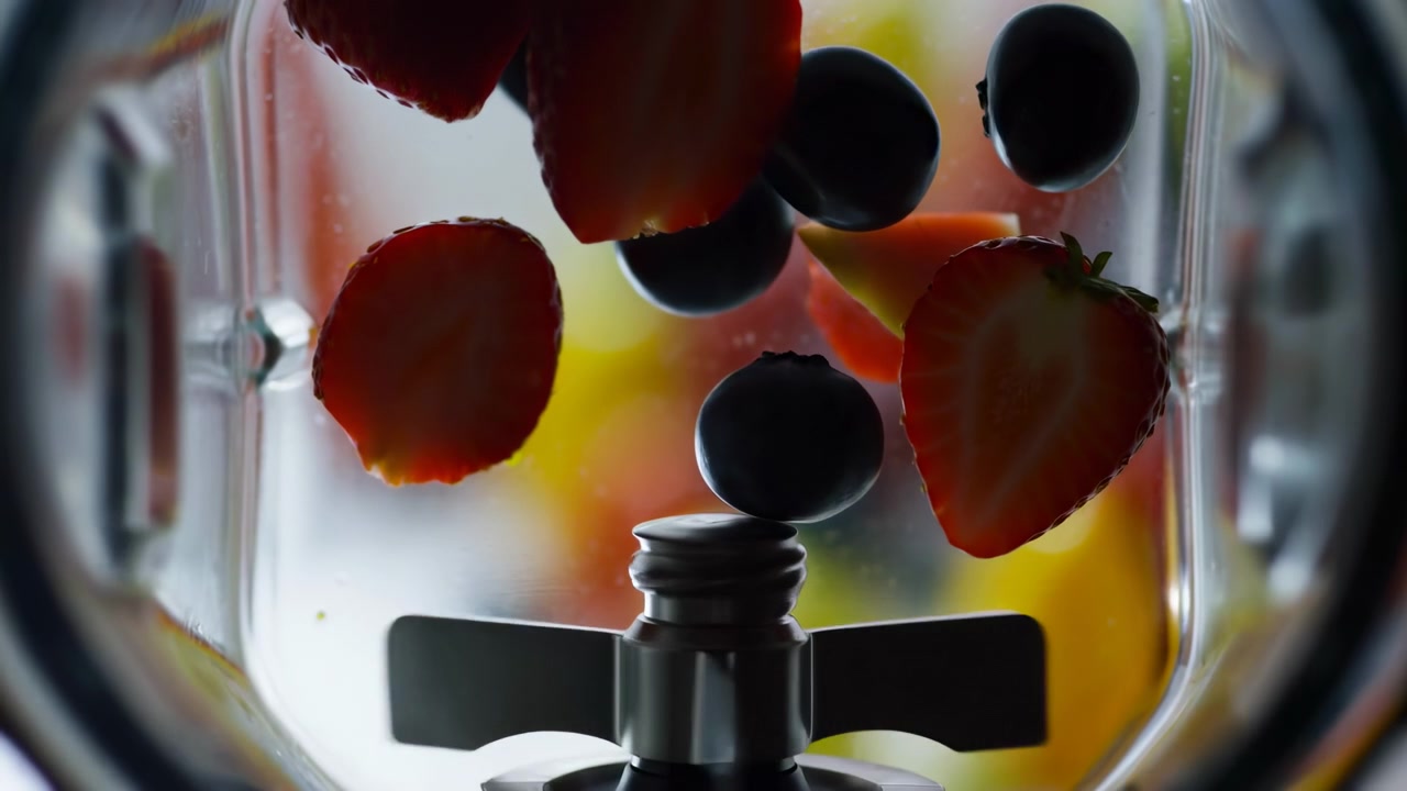 Close view from inside transparent blender jar shows strawberries, blueberries, and citrus pieces hovering around blade assembly, with glossy surfaces, warm backlight, and fresh vibrant food mood