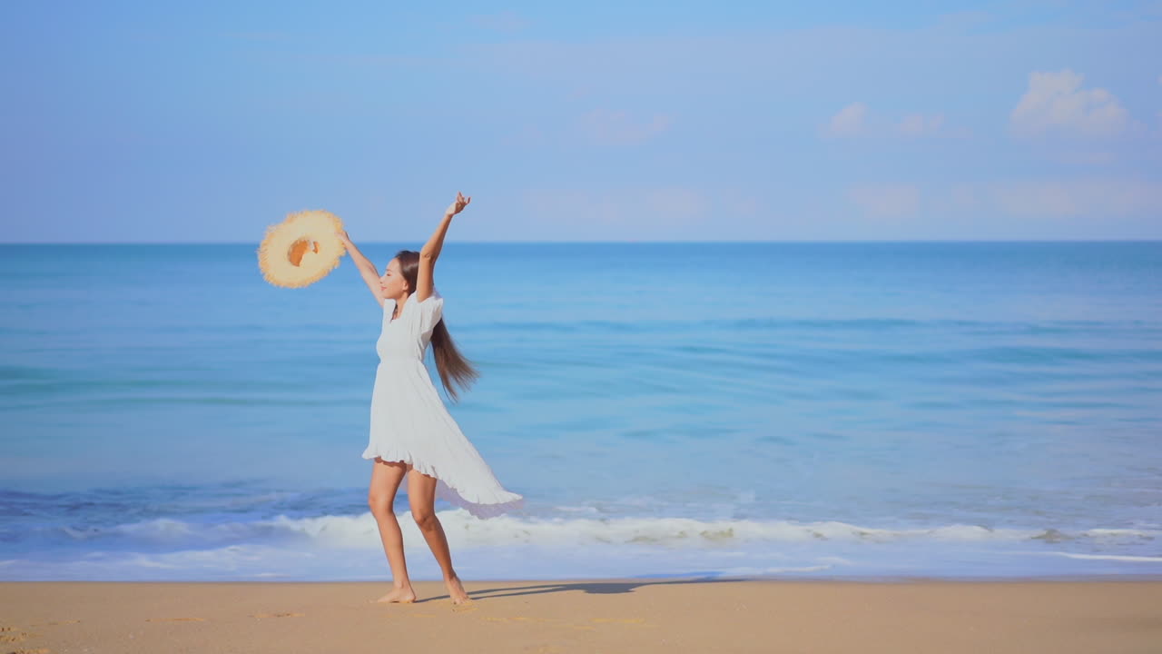 모래사장을 따라 바다를 향해 걷는 예쁜 젊은 여성이 원을 그리며 빙글빙글 돌면서 기쁨에 반응합니다.