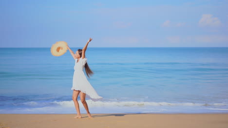 a pretty young woman walking along a sandy beach toward the sea reacts in joy by twirling around in circles