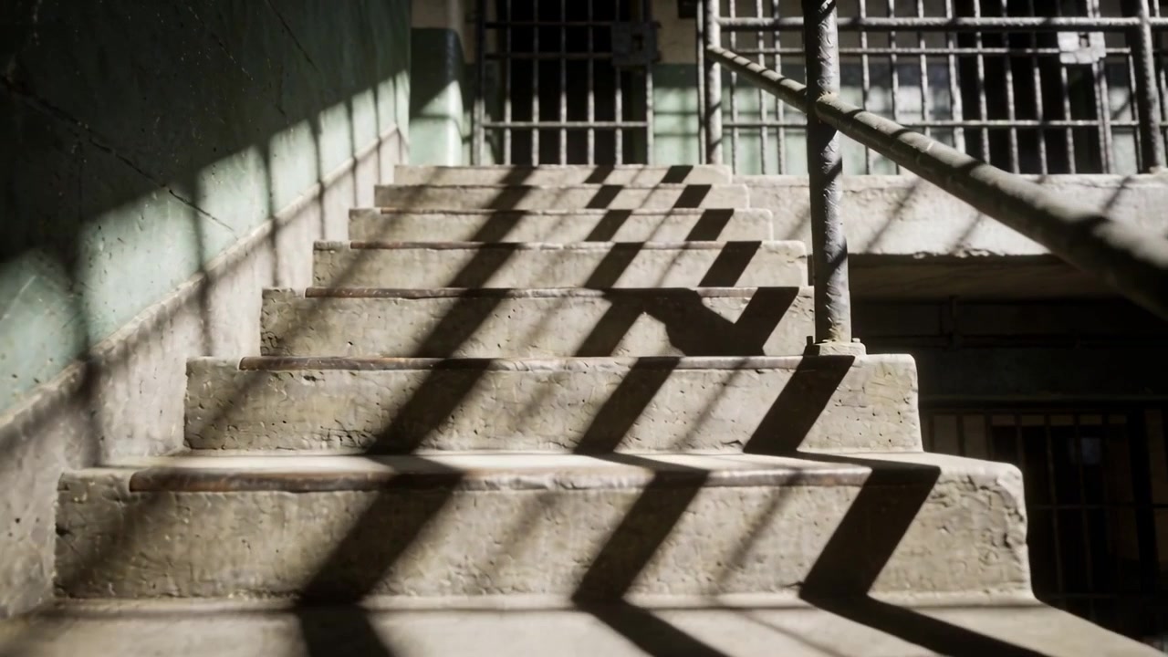 Pouring sun through bars in stairwell casting moving shadows up across concrete stairs with rail