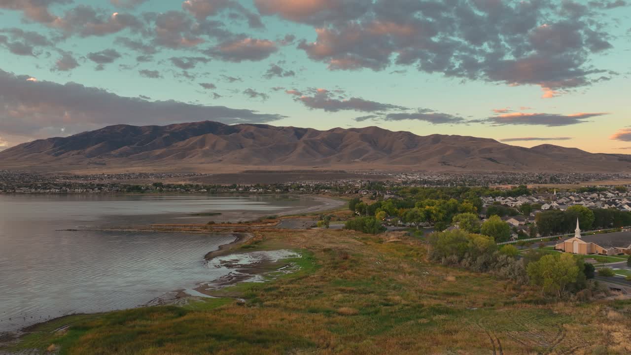 Aerial footage captures the serene Utah Lake shoreline at sunrise in Saratoga Springs with a seamless push towards Flat Top Mountain, showcasing vibrant lighting and picturesque landscapes
