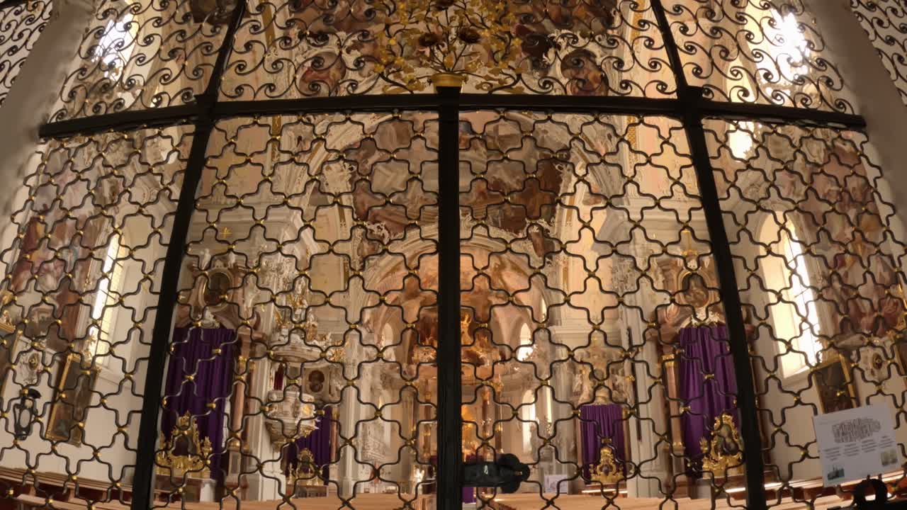 Interior detail of the basilica in Innsbruck showing an elaborate wrought iron screen with golden accents and Baroque ornamentation, separating the main nave from the sanctuary area
