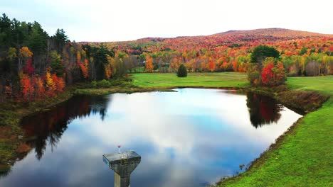 vivid autumn landscape, blue pond water with sky mirror reflection and colorful forest foliage, drone aerial view