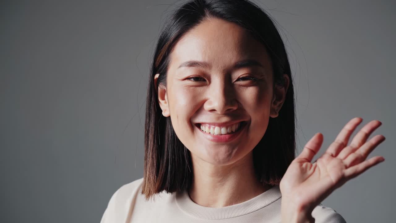 Close-up video of a smiling woman against a neutral background, shot with a straight-on camera
