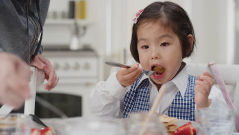 cute little asian girl eating breakfast father preparing waffles for daughter enjoying delicious homemade meal in kitchen at home getting ready for school 4k