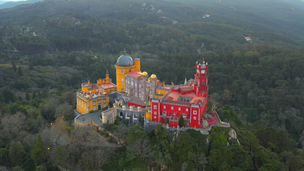 Uitzoomende luchtopname van het kleurrijke Paleis van Pena op een steile heuvel omgeven door bos, Sintra