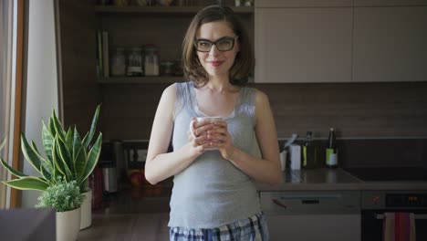 smiling woman standing in kitchen holding cup