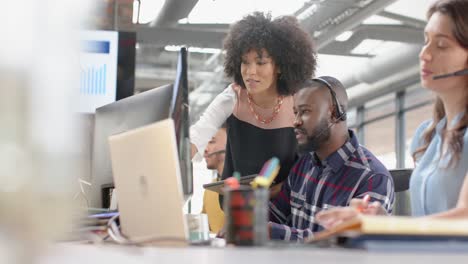 Happy-diverse-businesspeople-discussing-over-a-computer-at-desk-in-office