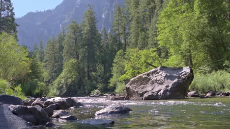 low-angle footage skims the surface of the merced river as it races around a house-sized granite boulder
