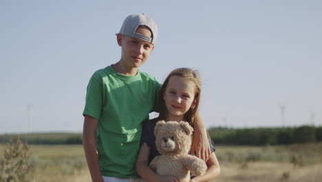 siblings with teddy bear in a field