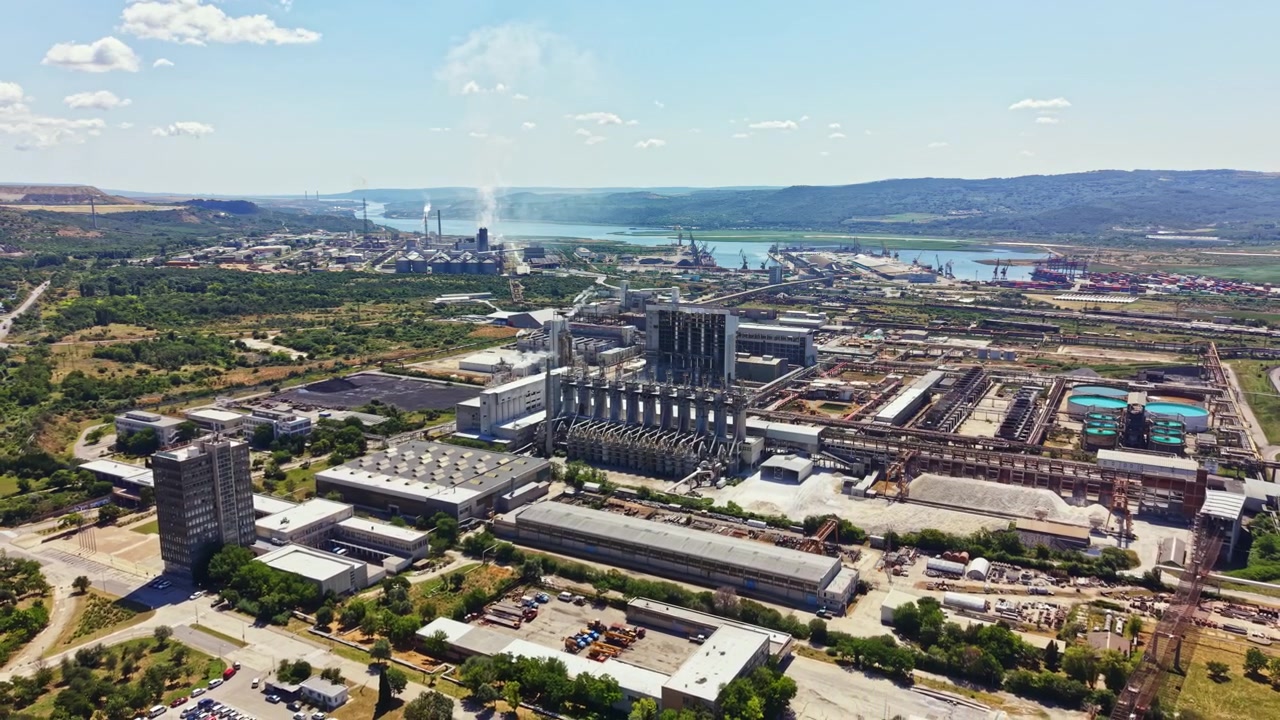 Gran zona industrial cerca de un río con múltiples fábricas y zonas verdes, tomada durante el día con cielos despejados y algunas nubes