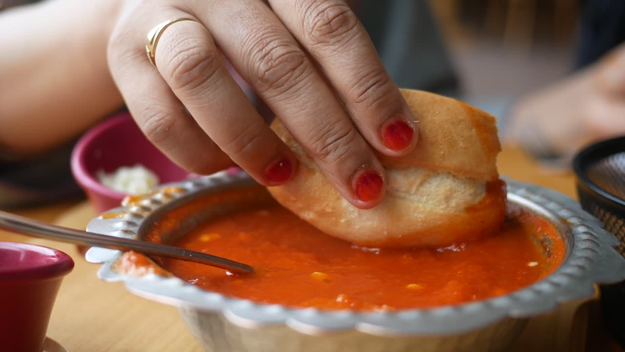 A Person Dipping Bread Into Tomato Soup