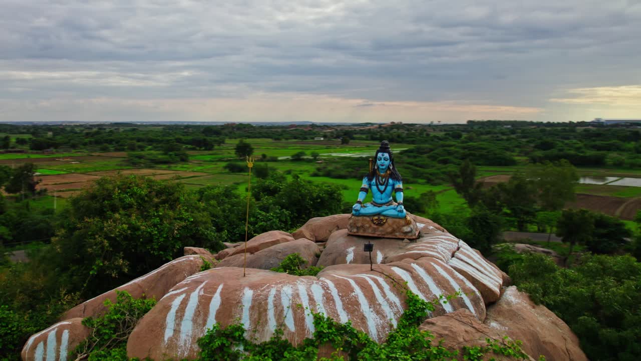 lord shiva statue with granite stone in the background crop fields lands and temple, orbit shot, drone shot, 4k.