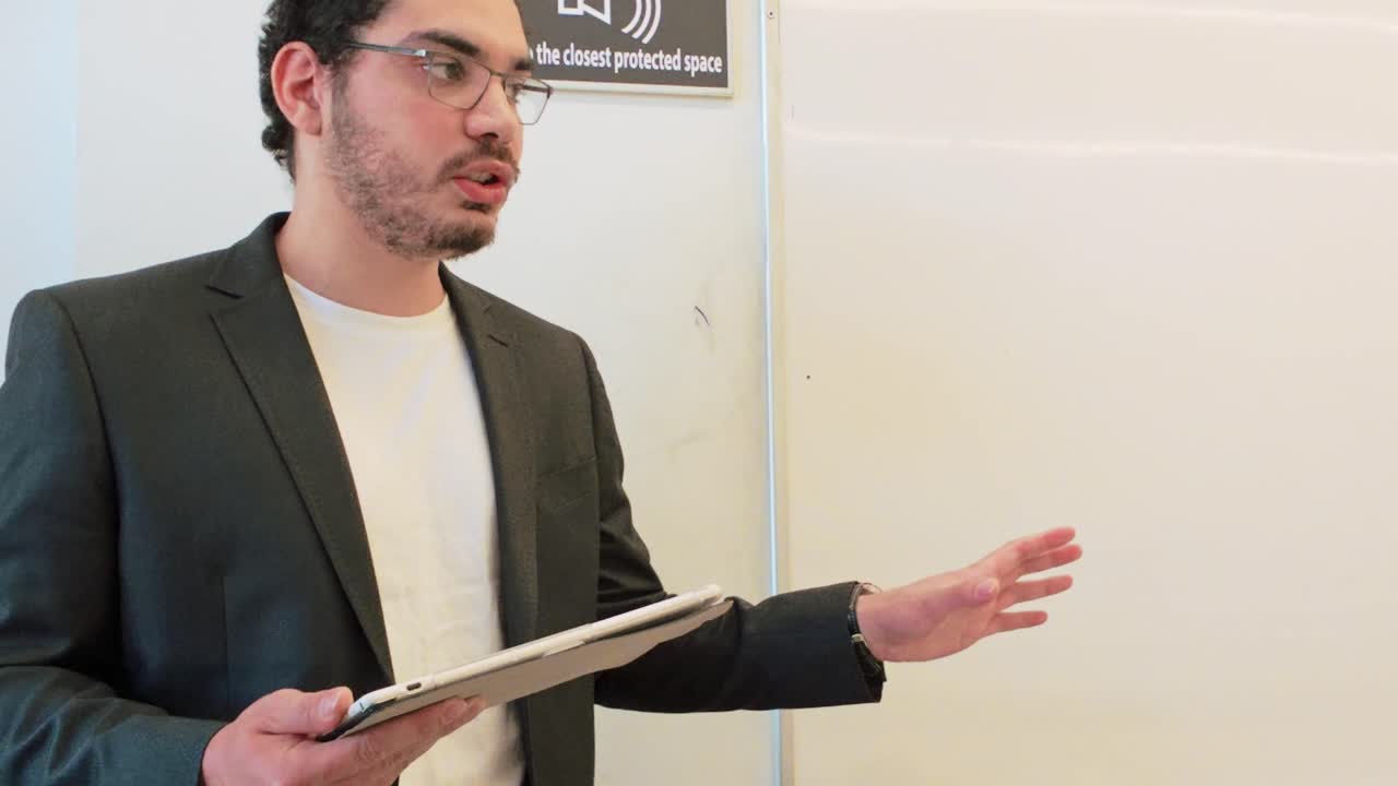 Young man in a blazer and t-shirt, holding a tablet, delivers a business casual presentation