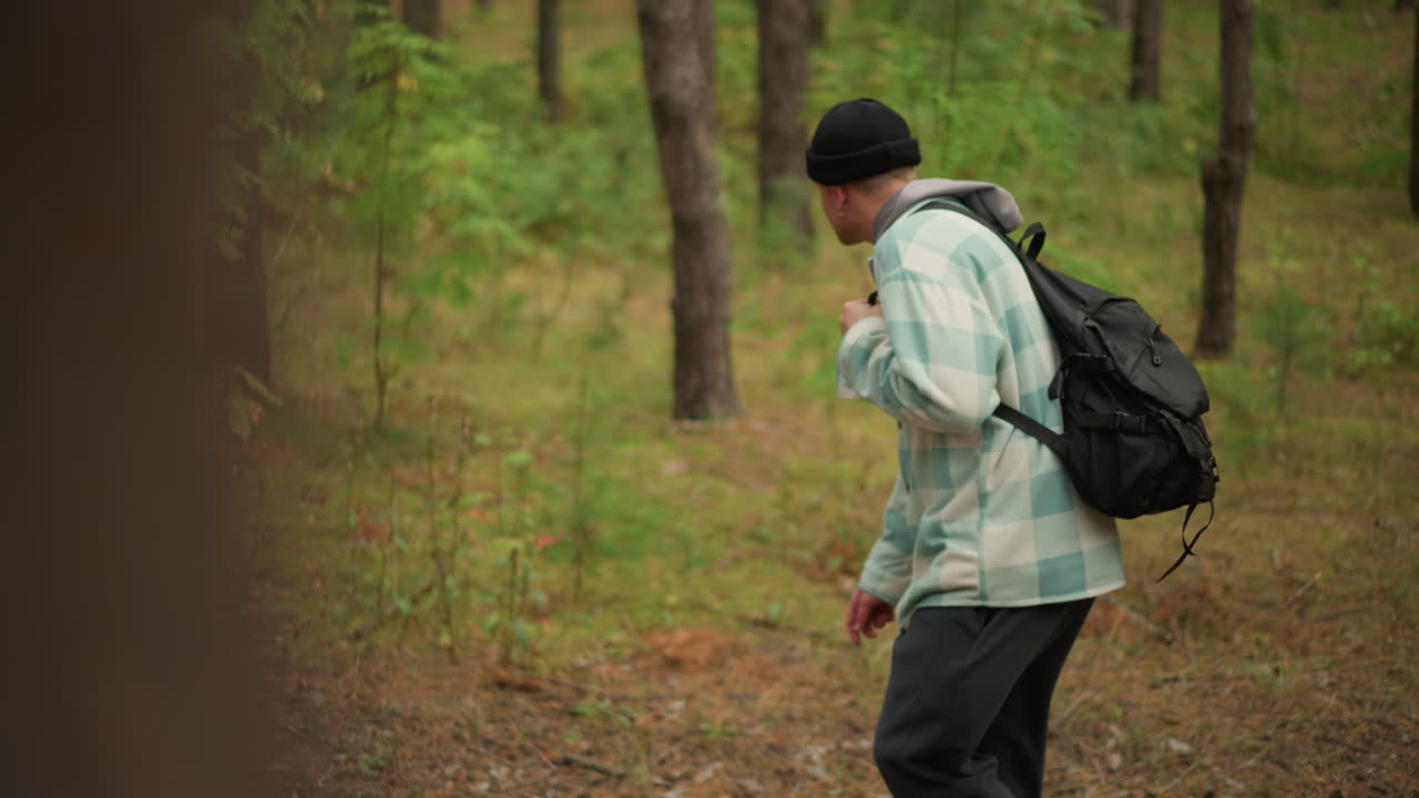 Caucasian hiker walking through pine forest, peeking behind trees and scanning trail while adjusting backpack scout, observer, navigator roles across frames quiet microadventure mood, soft overcast