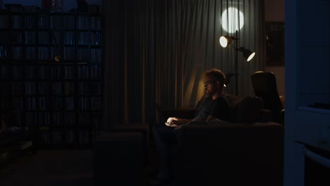 wide view of a workaholic man working on his laptop in his living room