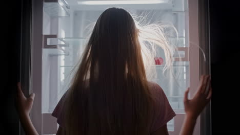 a young girl takes out one red apple from an empty refrigerator. proper nutrition and diet concept