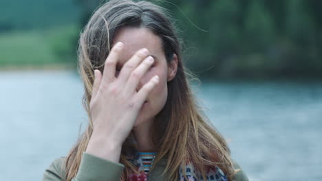 portrait independent young woman looking confident with serious expression running hand through hair with wind blowing outdoors by lake 4k