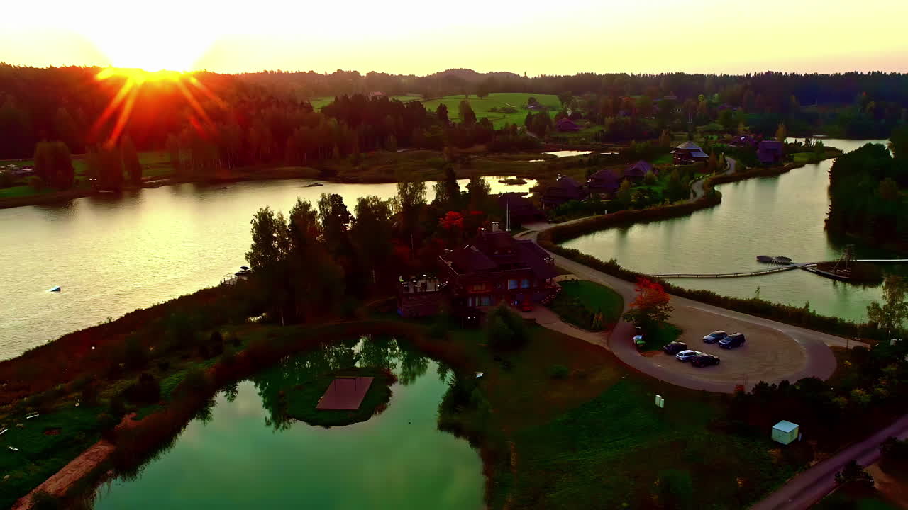 라트비아 자연의 아름다운 일몰 시간 동안 주택이 있는 천연 호수 리조트의 공중 역방향 촬영 - amatciems, amata,europe
