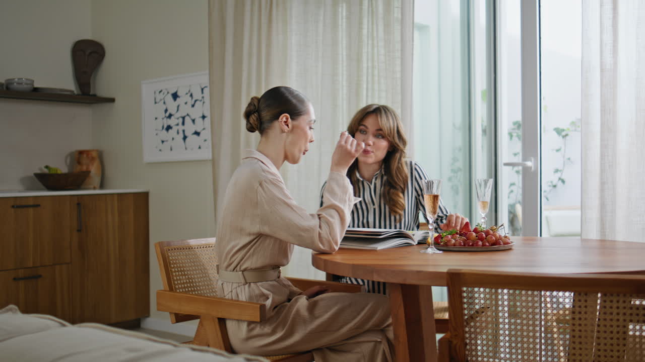 Two ladies discussing fashion style looking magazine on kitchen. Women talking