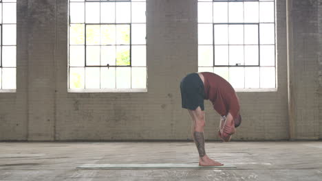 man in an industrial warehouse practicing yoga, the pose of forward fold.