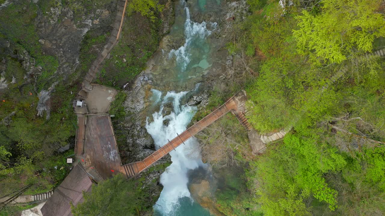 Veduta aerea dall'alto di una cascata con un ponte che la attraversa, avvolta da una vegetazione lussureggiante.