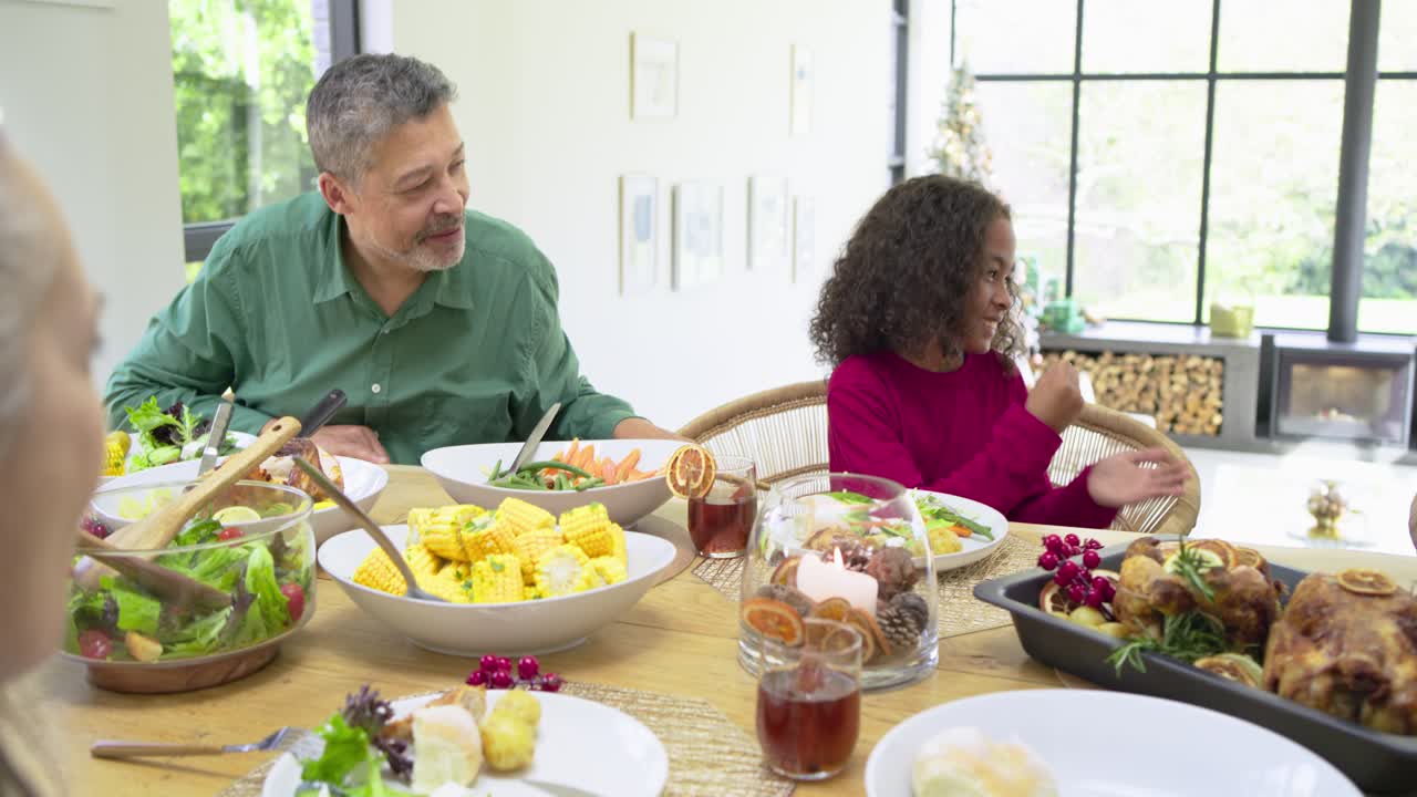 Diverse sisters fist bumping as father placing hand on daughter before eating salad at dining table