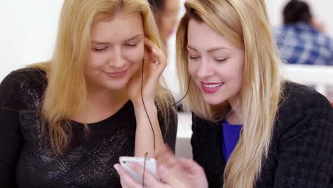Two young girls watches video on smartphone and relaxing in cafe