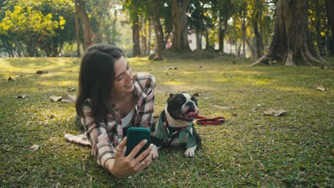 woman taking a selfie with her boston terrier in a park
