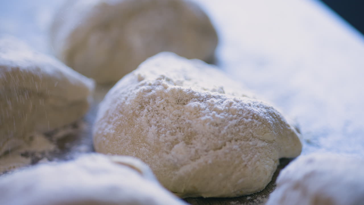 테이블 위의 반죽 조각에 밀가루를 뿌리는 손 클로즈업