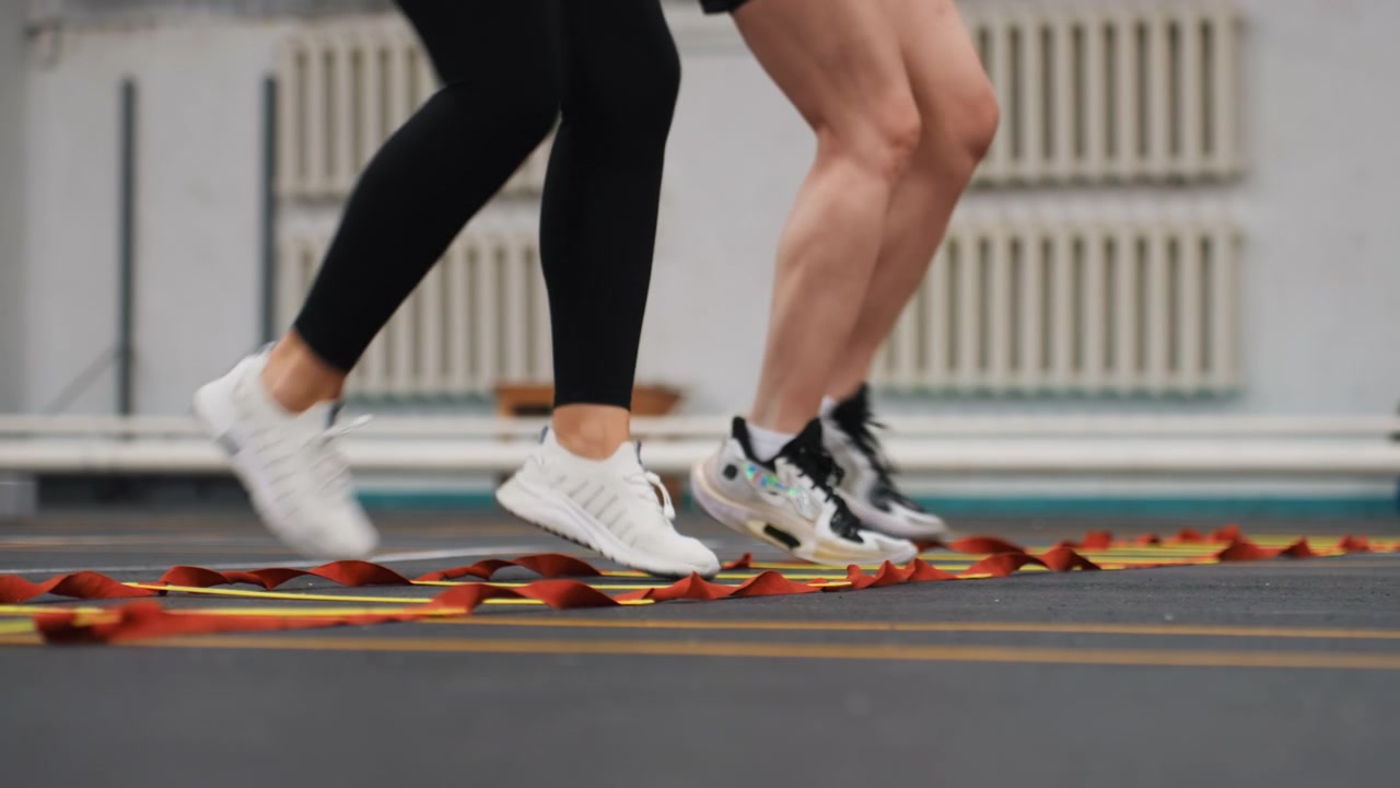 Riscaldamento ritmico con scaletta per giocatori di badminton, duo che esegue salti sincronizzati e esercizi di passo rapido sulla scaletta di agilità, scarpe che strisciano sulla superficie del campo, ritmo vivace e focus sulla resistenza