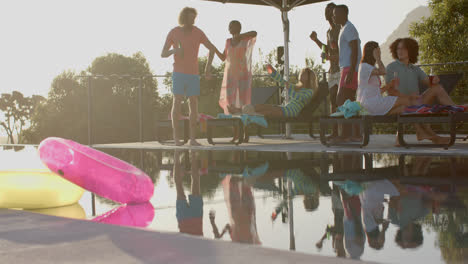 happy diverse friends with drinks talking and dancing in the setting sun at pool party, slow motion