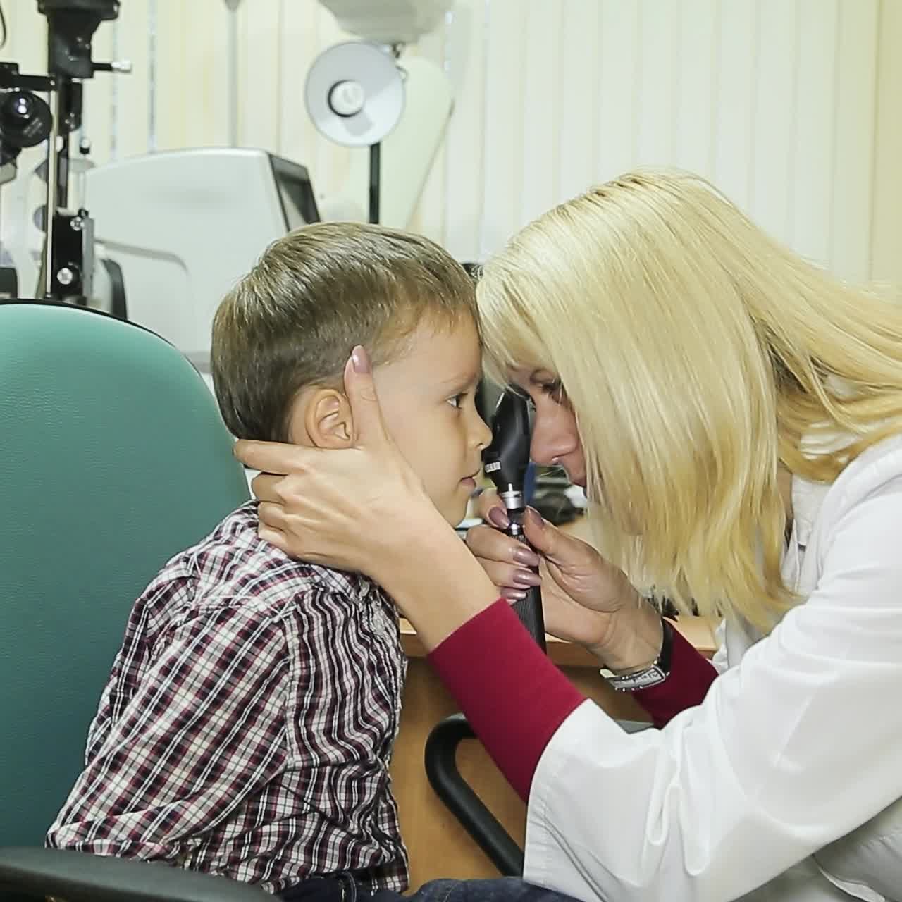Side view of female pediatric optometrist examining eyes of little boy. Children ophthalmology
