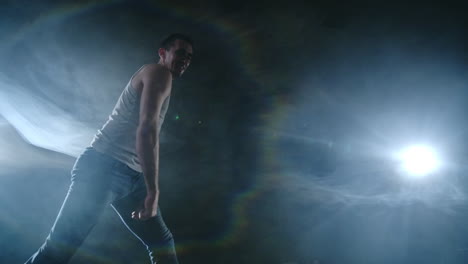 modern ballet a man from a sitting position on the stage jumps somersault with rotation to the camera on a dark stage in the smoke in the spotlight. modern choreography on the stage of the theater. dance show.