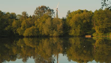 Lago-Tranquilo-Al-Amanecer-Con-Energía-Verde-De-Turbina-Eólica-Con-Luz-De-Hora-Dorada---Cámara-Lenta