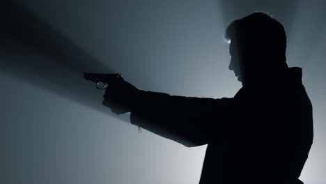 silhouette male shooter aiming pistol in darkness. criminal man raising hand gun