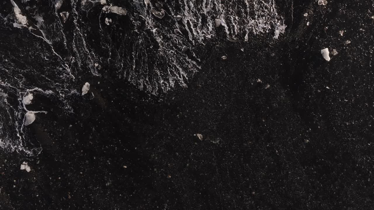 Diamond Beach near Jökulsárlón glacier lagoon, aerial top-down view of luminous icebergs on volcanic black sand during sunrise.