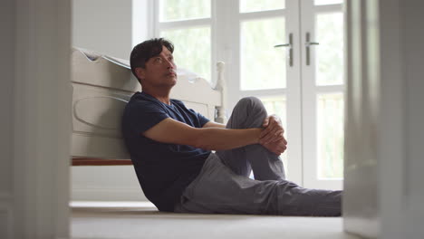 Unhappy-and-depressed-mature-Asian-man-wearing-pyjamas-sitting-on-floor-in-bedroom---shot-in-slow-motion