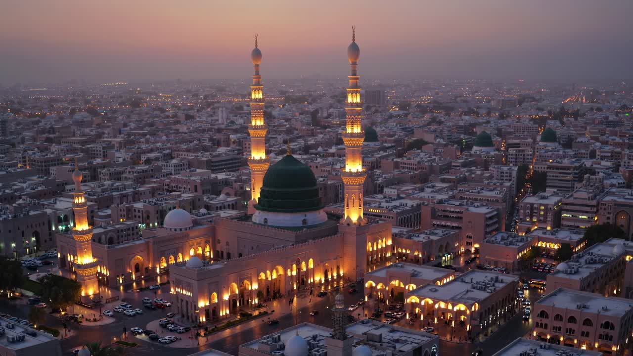 Majestic mosque with glowing minarets and a green dome stands prominently amidst a sprawling cityscape at sunset, exuding tranquility and spiritual significance