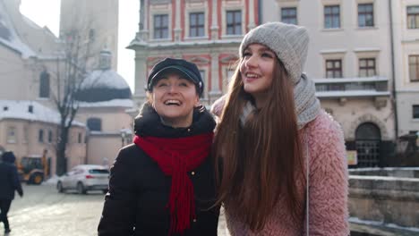 Two-smiling-women-tourists-walking-together-on-city-street,-family-couple-talking,-embracing