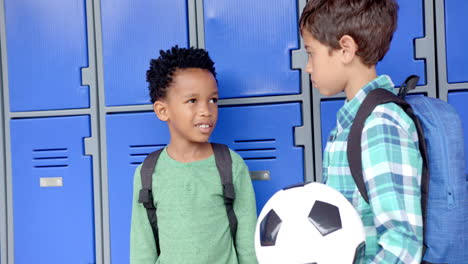 in school, two boys with backpacks talking near lockers, holding soccer ball