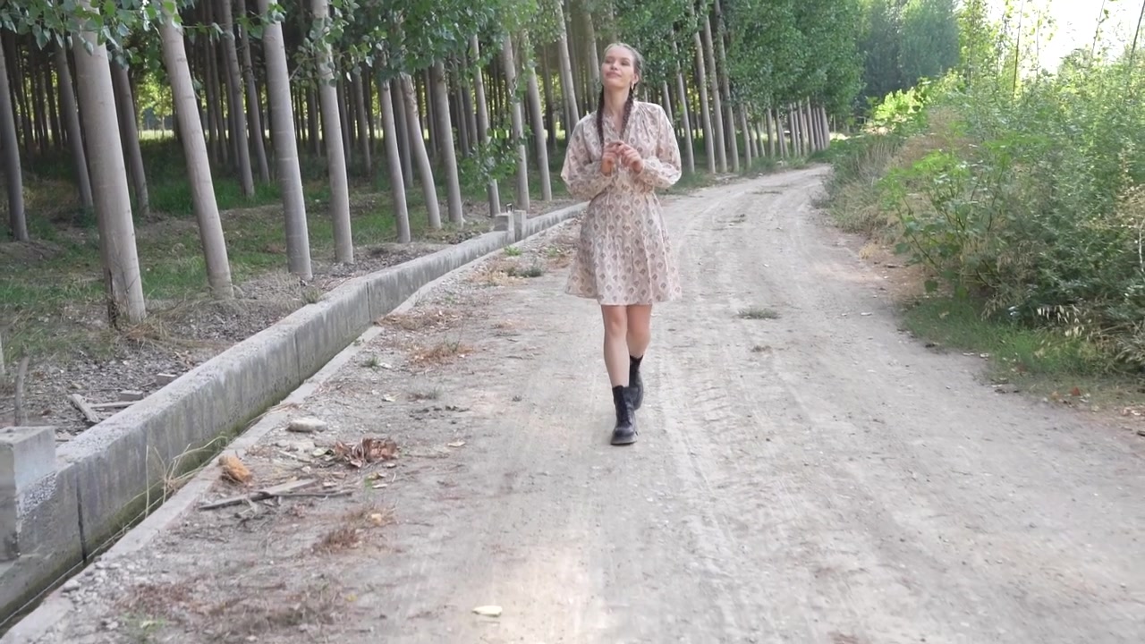 Una giovane donna che passeggia lungo un sentiero tranquillo, avvolta da alberi alti e rigogliosi e dalla natura.