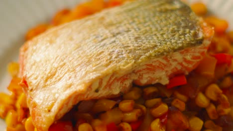 top view of salmon with crispy skin resting on bed of peppers and sweetcorn in natural light. healthy omega-3 rich seafood after cooking and plating