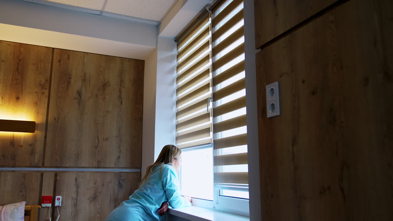 Caucasian woman stands leaned on the window-sill looking into window. Future mom in the maternity hospital ward.