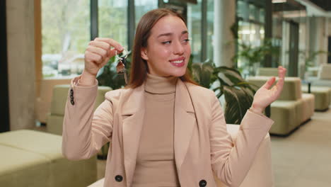 caucasian young businesswoman real estate agent showing the keys of new home in office lobby